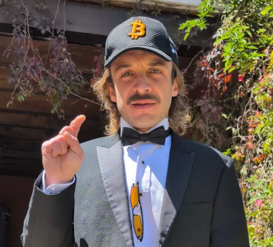 Guatemalan investor José T. wearing a Bitcoin cap and a tuxedo, raising a finger to make a point